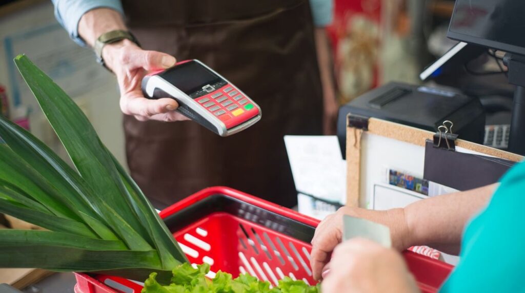 Оплата покупок карткою на касі невеликого продуктового магазину, кошик із зеленню